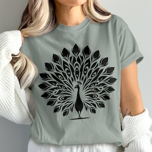 May include: Sage green t-shirt featuring a black peacock design. The peacock is depicted with its tail feathers fully displayed. The graphic is centered on the shirt, creating a bold and eye-catching design. The shirt has short sleeves.