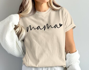 Puede incluir: Camiseta beige con la palabra "mama" en escritura negra, un corazón reemplaza la letra "a". La camiseta tiene mangas cortas y un corte relajado. La camiseta está hecha de un material suave.