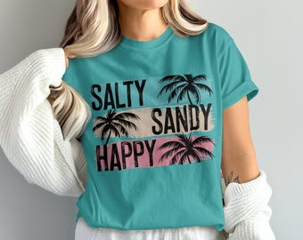 May include: Teal t-shirt with the words "SALTY SANDY HAPPY" in black, each word above a palm tree graphic. The words are on horizontal color blocks of black, tan, and pink. The shirt is a short-sleeved crew neck.