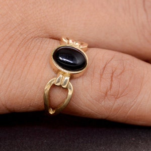 Puede incluir: Un anillo dorado con una piedra preciosa negra ovalada. El anillo tiene un diseño único con apariencia de cadena. El anillo se lleva en un dedo, mostrando su estilo elegante y clásico. El anillo es una pieza de joyería.