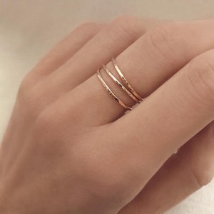 Puede incluir: Tres delicados anillos de oro rosa apilados en un dedo. Cada anillo tiene una textura martillada, que capta la luz. Los anillos son simples y elegantes, adecuados para el uso diario. Los anillos son de un color metálico cálido.