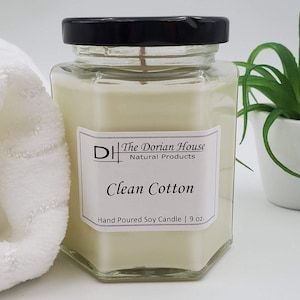 May include: A glass jar candle with a black lid and a white label. The label reads "The Dorian House Natural Products" and "Clean Cotton". The candle is hand-poured soy and is 9 ounces.