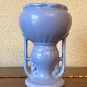 May include: A light blue ceramic vase with a scalloped rim and two handles. The vase has a bulbous body and a flared base.