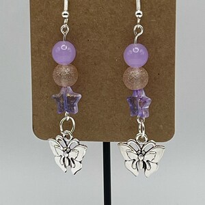 May include: A pair of silver dangle earrings with a purple and pink bead, a star charm, and a butterfly charm.