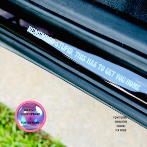 May include: A black car door sill with a white vinyl decal that reads "Remember stupid, this has to get you home". The decal is surrounded by a blue iridescent circle with the text "Over 50+ Color Options & Font Options". The font used is Daylight, color: Ice Blue.