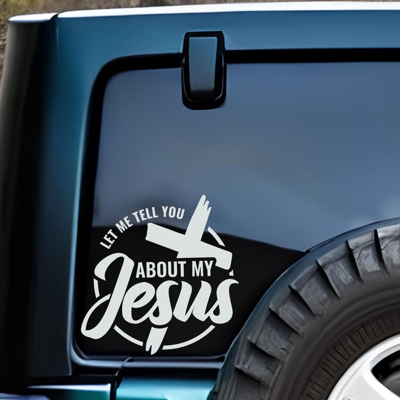 May include: White vinyl decal with a cross and the text "Let me tell you about my Jesus" in a circle on a black background. The decal is on the back window of a blue car.