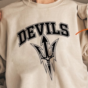 May include: Beige sweatshirt with the word "DEVILS" in black block letters above a black trident graphic. The sweatshirt design is also shown on a round graphic with the text "SVG PNG Instant Download".