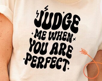 May include: A white t-shirt with black text that reads "JUDGE ME WHEN YOU ARE PERFECT" and a black hand with a middle finger up with the text "DON'T JUDGE ME". There is also a smaller version of the t-shirt design with the text "JUDGE ME WHEN YOU ARE PERFECT".