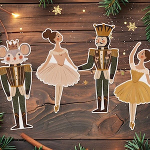 Puede incluir: Cuatro adornos navideños sobre una superficie de madera. Los adornos representan personajes del ballet El Cascanueces: un rey ratón, dos bailarinas y un soldado cascanueces. Los adornos son en tonos marrón, verde y dorado, con toques de blanco y rosa.