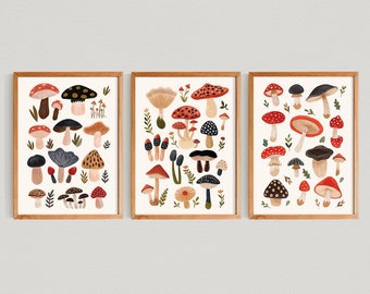 May include: Three framed art prints featuring colorful mushroom illustrations. The mushrooms are depicted in various shapes and sizes, with red, brown, black, and tan caps. The prints are set against a cream background, with a wooden frame.
