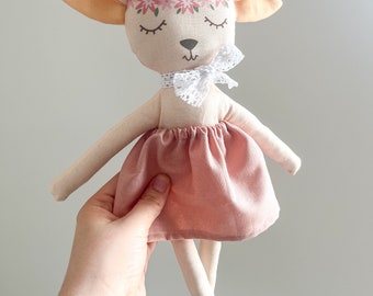 May include: A handmade plush toy in the shape of a lamb with a pink floral headband, closed eyes, and a pink skirt. The lamb is holding a white lace bow.