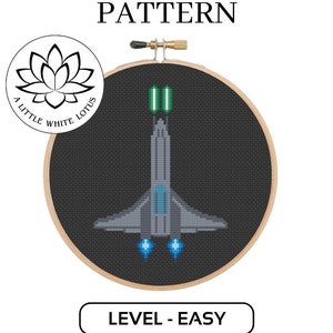 Puede incluir: Un patrón de punto de cruz de una nave espacial con luces verdes y azules, en un aro de bordado de madera. El patrón está etiquetado como "Nivel - Fácil" y es un producto de descarga digital compatible con el software Pattern Keeper.