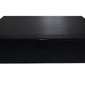 May include: A rectangular black box with a hinged lid. The box is made of a smooth, matte material and features a subtle clasp on the front. The design is simple and elegant, suitable for storage or display.