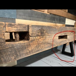 May include: A rustic, reclaimed wood bench with a natural, weathered appearance. The bench features a thick, rectangular top with visible wood grain and knots. It is supported by black metal legs, creating a contrast between the wood and metal.