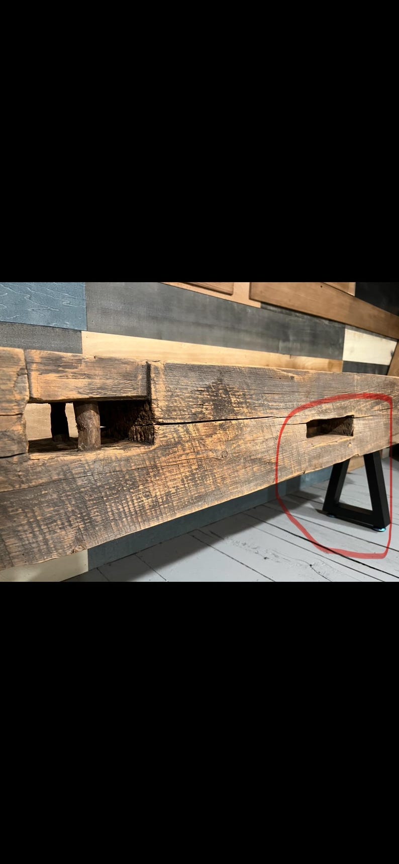 May include: A rustic, reclaimed wood bench with a natural, weathered appearance. The bench features a thick, rectangular top with visible wood grain and knots. It is supported by black metal legs, creating a contrast between the wood and metal.