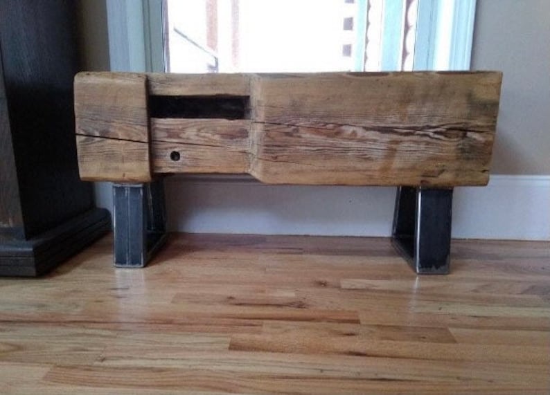 May include: A rustic wooden bench with a natural finish, featuring a built-in drawer and supported by two dark metal legs. The bench is made from reclaimed wood, showcasing visible grain and knots.