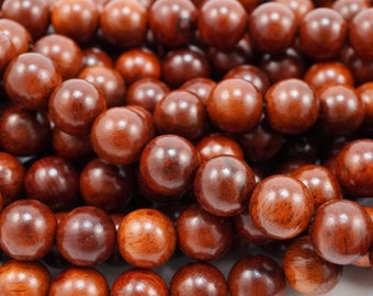 Puede incluir: Primer plano de un montón de cuentas redondas de madera marrón oscuro. Las cuentas son lisas y pulidas, con una veta de madera natural visible.
