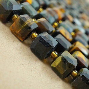 May include: A close-up of a necklace made of dark blue and gold tiger's eye gemstone beads. The beads are faceted and have a geometric shape.