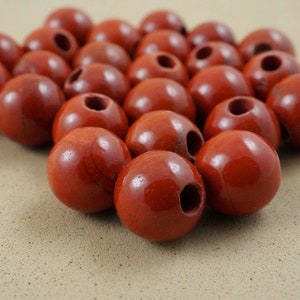 May include: A group of round, red beads with a hole through the center. The beads are made of a smooth, polished material and have a glossy finish.