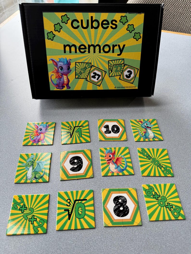 May include: A black box with the words "cubes memory" and a cartoon dragon. Twelve square cards with dragon illustrations and math problems are scattered in front of the box. The cards have green and yellow striped backgrounds.