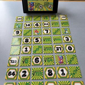 May include: A memory game set with a black box labeled "cubes memory" and colorful hexagonal cards. The cards feature numbers, cube roots, and illustrations of a dragon. The game is designed for educational purposes.