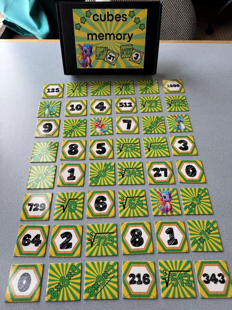 May include: A memory game set with a black box labeled "cubes memory" and colorful hexagonal cards. The cards feature numbers, cube roots, and illustrations of a dragon. The game is designed for educational purposes.