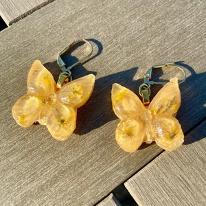 Brincos pendentes de borboleta amarela com pequenas flores amarelas reais envoltas em resina ecológica