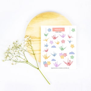 May include: A sheet of colorful origami crane and star stickers. The stickers are arranged in rows and feature a variety of pastel colors. The sheet is labeled "milkyco. origami doodles".