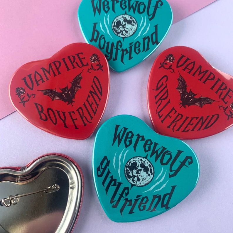 May include: Four heart-shaped pins with different designs. Two red pins say "Vampire Boyfriend" with a bat graphic. Two teal pins say "Werewolf Boyfriend" and "Werewolf Girlfriend" with a moon graphic.