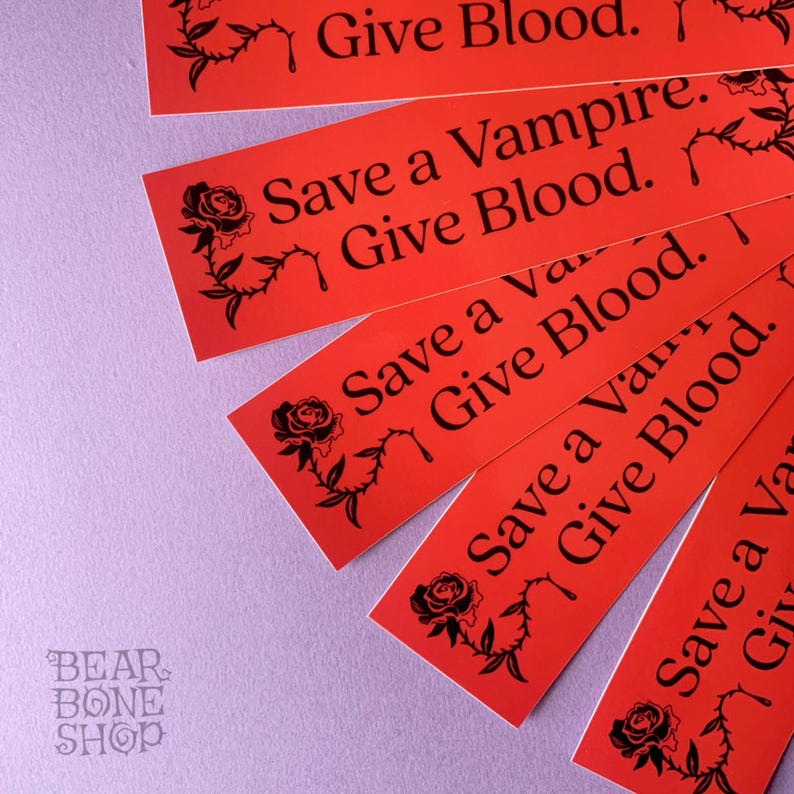 May include: Five red stickers with black text and a black rose graphic. The text on the stickers reads "Give Blood." "Save a Vampire. Give Blood." "Save a Vampire. Give Blood." "Save a Vampire. Give Blood." and "Save a Vampire. Give Blood."