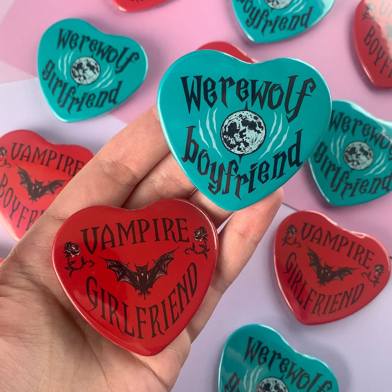 May include: A set of heart-shaped pins with various designs. The pins feature a full moon, bat, and text that reads "Werewolf Boyfriend", "Werewolf Girlfriend", "Vampire Boyfriend", and "Vampire Girlfriend".