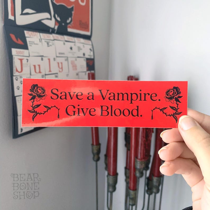 May include: Red sticker with black text and a black rose design. The text reads "Save a Vampire. Give Blood."