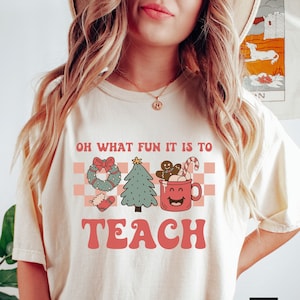 May include: Ivory t-shirt with a red and green Christmas themed graphic that says "Oh what fun it is to teach".
