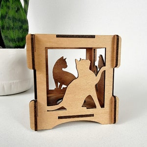 May include: Wooden cat-themed decorative box. The box features a rectangular frame with cut-out silhouettes of cats. The cats are in various poses, adding a playful touch. The natural wood color gives it a rustic feel.
