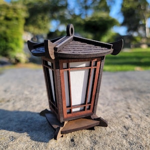 May include: A small wooden lantern with a dark brown finish and a white paper insert. The lantern has a traditional Japanese design with a curved roof and intricate details.