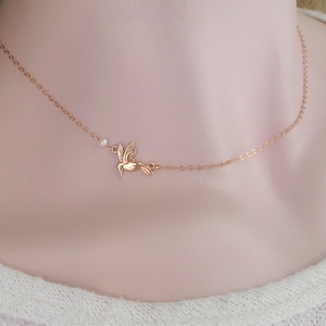 May include: A delicate rose gold necklace with a small hummingbird charm and a single pearl accent.