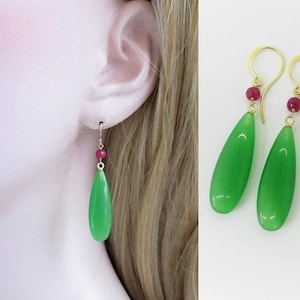 以下が含まれることがあります： 緑色の宝石のドロップイヤリングに、小さな赤い宝石のアクセントが施されています。イヤリングは金製です。