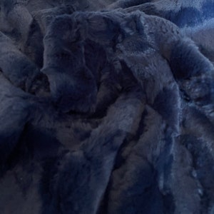 May include: A close-up shot of a navy blue faux fur blanket. The plush fabric is soft and textured, with visible folds and shadows that create depth. The blanket appears to be thick and warm, perfect for snuggling.