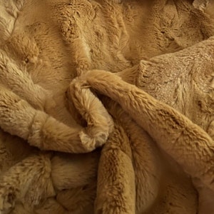 May include: A close-up of a soft, brown faux fur fabric. The fabric has a fluffy texture and a subtle sheen.