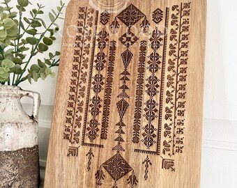 May include: A wooden cutting board with a decorative geometric pattern engraved on the surface. The pattern is in a dark brown color and resembles traditional embroidery.