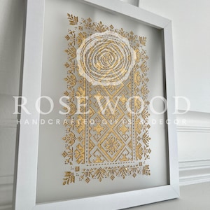 K&ouml;nnte beinhalten: Ein wei&szlig; gerahmtes Wandbild mit einem goldenen geometrischen Design. Das Design zeigt einen zentralen Kreis mit komplizierten Mustern, die nach au&szlig;en strahlen. Der Text "ROSEWOOD HANDCRAFTED GIFTS & DECOR" ist am unteren Rand des Bildes sichtbar.