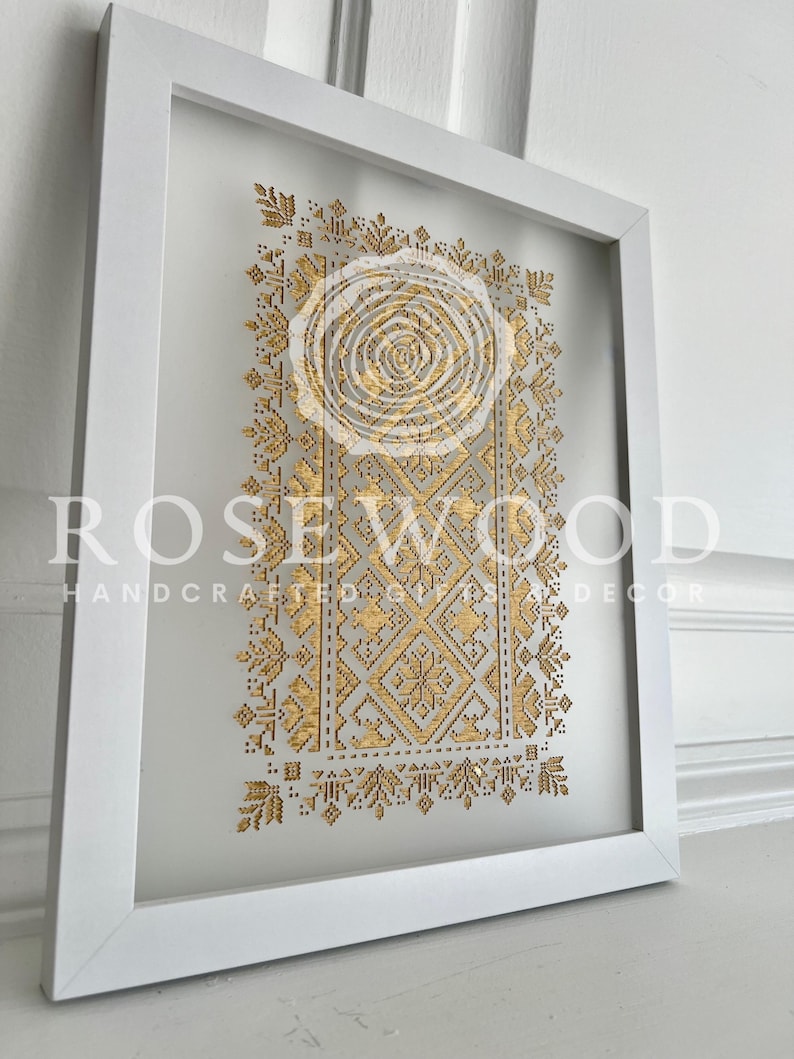 K&ouml;nnte beinhalten: Ein wei&szlig; gerahmtes Wandbild mit einem goldenen geometrischen Design. Das Design zeigt einen zentralen Kreis mit komplizierten Mustern, die nach au&szlig;en strahlen. Der Text "ROSEWOOD HANDCRAFTED GIFTS & DECOR" ist am unteren Rand des Bildes sichtbar.