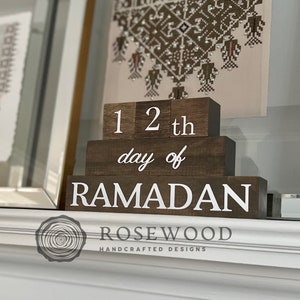 May include: Wooden Ramadan countdown blocks. The blocks are dark brown with white lettering that reads "12th day of Ramadan". The blocks are stacked on top of each other. The Rosewood logo is at the bottom.