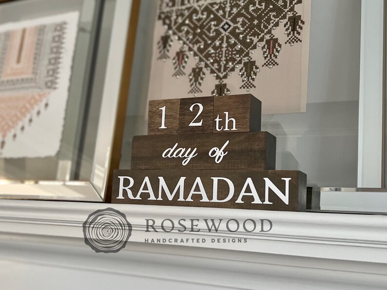 May include: Wooden Ramadan countdown blocks. The blocks are dark brown with white lettering that reads "12th day of Ramadan". The blocks are stacked on top of each other. The Rosewood logo is at the bottom.