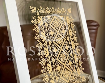 May include: A white framed picture with a gold geometric pattern inside. The pattern is a traditional Ukrainian design. The frame is made of wood and has a glass front.