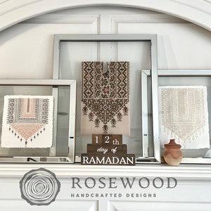 May include: A display of framed art pieces with mirrored frames, featuring intricate textile designs in neutral tones. A wooden block reads "12th day of RAMADAN". A candle and decorative vase complete the arrangement. The Rosewood Handcrafted Designs logo is visible.
