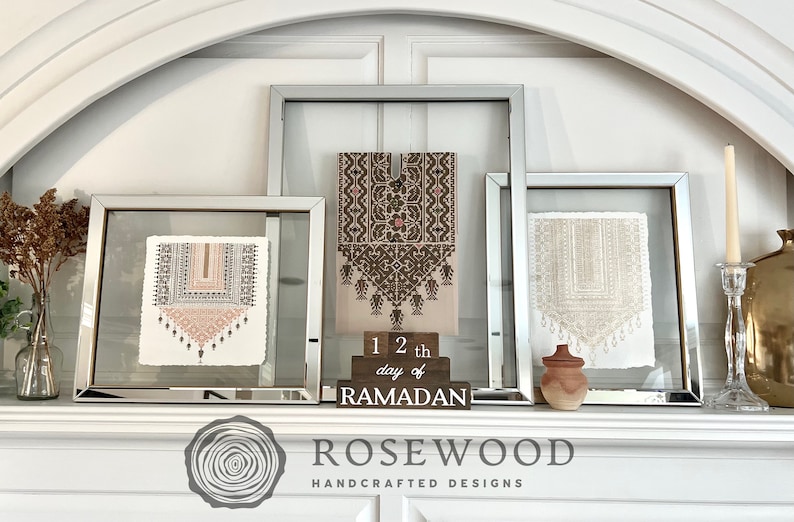 May include: A display of framed art pieces with mirrored frames, featuring intricate textile designs in neutral tones. A wooden block reads "12th day of RAMADAN". A candle and decorative vase complete the arrangement. The Rosewood Handcrafted Designs logo is visible.