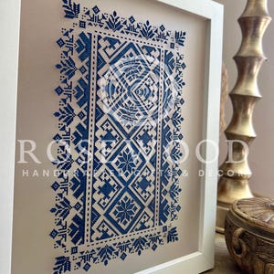 K&ouml;nnte beinhalten: Eine gerahmte blaue und wei&szlig;e geometrische Muster-Kreuzstich-Stickerei. Die Stickerei befindet sich in einem wei&szlig;en Rahmen mit einer beigefarbenen Passepartout. Der Text "ROSEWOOD HANDCRAFTED & DECOR" ist in der unteren rechten Ecke des Bildes sichtbar.