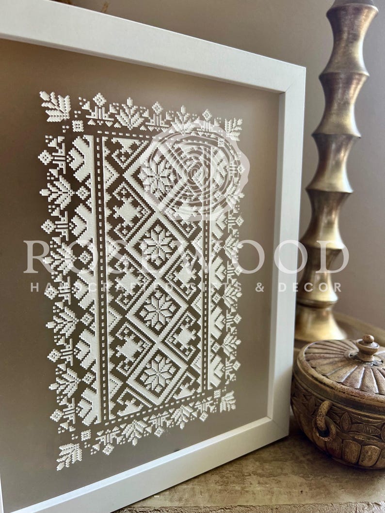 K&ouml;nnte beinhalten: Ein wei&szlig;er gerahmter Druck mit einem geometrischen Muster in Wei&szlig; auf beigefarbenem Hintergrund. Das Muster ist ein traditionelles Volksdesign mit einem sich wiederholenden Motiv aus Quadraten und Rauten.