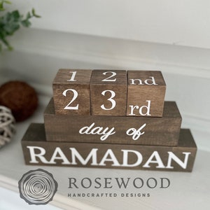 May include: Wooden Ramadan countdown blocks. The blocks are brown with white lettering. The top blocks display the numbers 1, 2, and 3, with "nd" and "rd" on the adjacent blocks. The bottom block reads "day of RAMADAN".